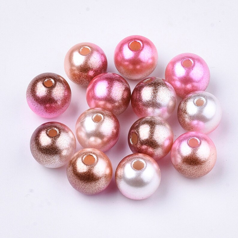 May include: A collection of round, iridescent beads in shades of pink and white. The beads have a pearlescent finish and are perfect for crafting jewelry or other decorative projects.