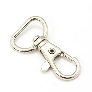 May include: Silver swivel clasp with a D-ring. The clasp is open and ready to be attached to a strap or chain.