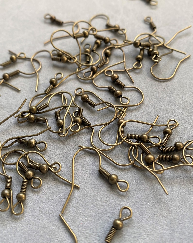 May include: A pile of gold-toned earring hooks with a spring-loaded closure. The hooks are made of metal and have a small ball at the end.