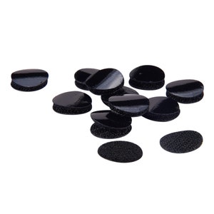 K&ouml;nnte beinhalten: Zehn schwarze runde Klebepads mit einer strukturierten Oberfl&auml;che. Die Pads sind auf einem wei&szlig;en Hintergrund verstreut.