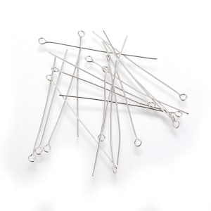 May include: A pile of silver head pins with loops on one end. The pins are scattered on a white surface.