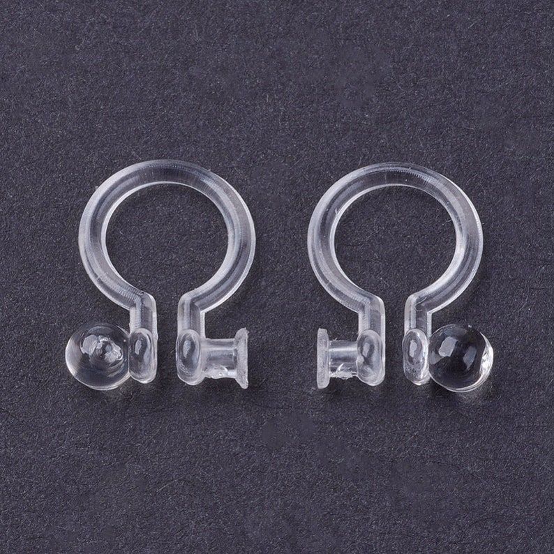 May include: A pair of clear plastic earring backs. The backs have a small, round, clear plastic ball on one end and a small, clear plastic loop on the other end.