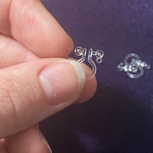 May include: A pair of clear plastic earring backs with small, round, clear beads. The earring backs are designed to be worn on the back of an earring to keep it in place.