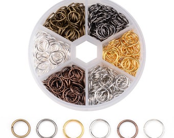 May include: A round plastic container with six compartments filled with jump rings in various colors: gold, silver, bronze, and black. The container is on a white background. There are six individual jump rings below the container, one of each color.