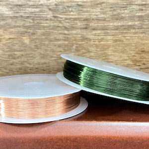 May include: Two spools of wire, one copper colored and one green, on a wooden surface.