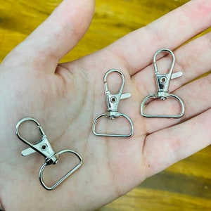 May include: Three silver metal swivel clasps with a spring-loaded gate. The clasps are commonly used for attaching keychains, lanyards, or other accessories.