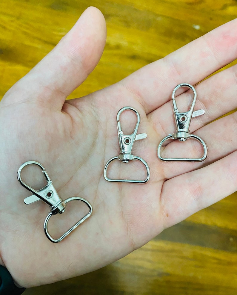 May include: Three silver metal swivel clasps with a spring-loaded gate. The clasps are commonly used for attaching keychains, lanyards, or other accessories.