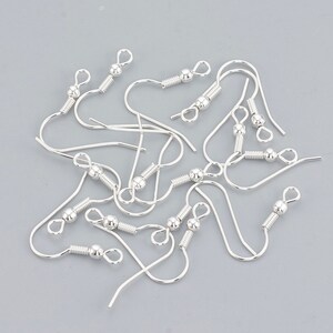 May include: A close-up of a group of silver earring hooks. The hooks are made of metal and have a small ball at the top. They are designed for making earrings.