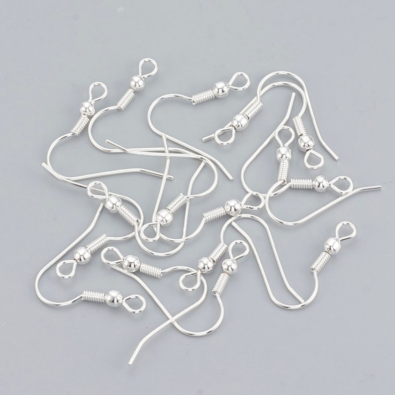 May include: A close-up of a group of silver earring hooks. The hooks are made of metal and have a small ball at the top. They are designed for making earrings.