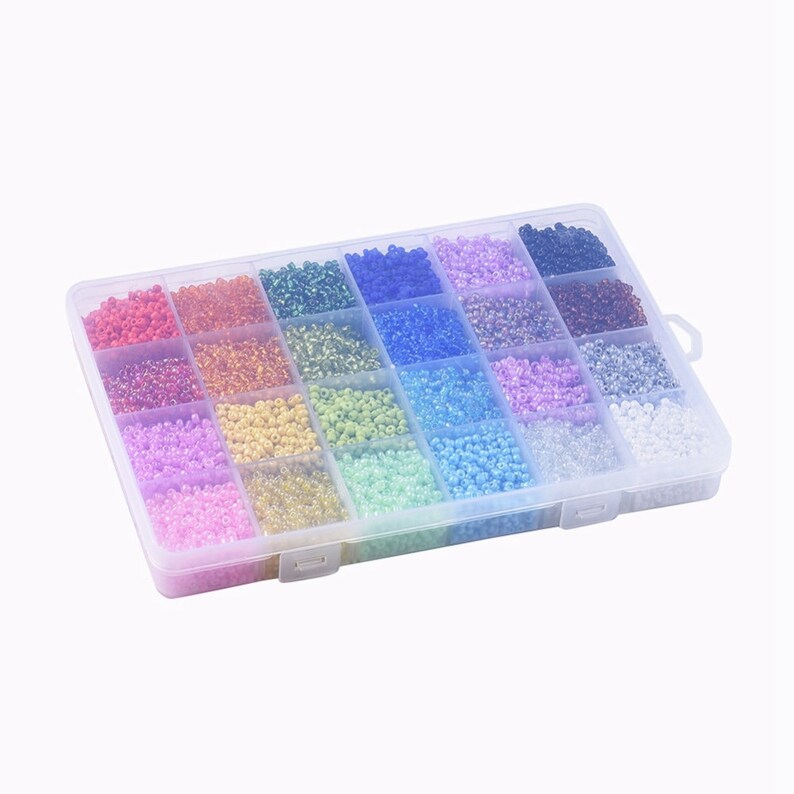 May include: A clear plastic storage box filled with 24 compartments, each containing a different color of seed beads. The beads are small and round, and they are arranged in a rainbow pattern.