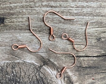 May include: Four copper earring hooks with a spring closure. The hooks are on a wooden surface.
