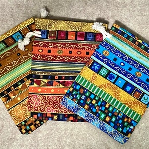 Può includere: Tre piccole borse con coulisse con motivi geometrici colorati. Le borse sono in tessuto e hanno un filo metallico dorato intrecciato nel design. Le borse sono in tonalità di blu, verde, arancione, rosso e marrone.