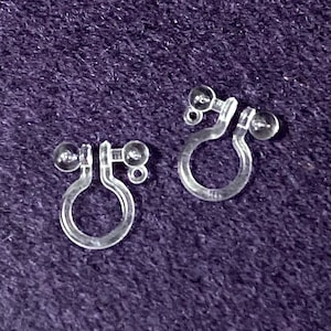 Puede incluir: Un par de respaldos de pendientes de plástico transparente con pequeñas bolas de plástico transparente en cada extremo.