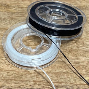 May include: Two spools of thread, one black and one white, are on a wooden surface. The thread is wound around clear plastic spools.