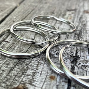 May include: A set of five silver key rings, stacked on top of each other, on a wooden surface.