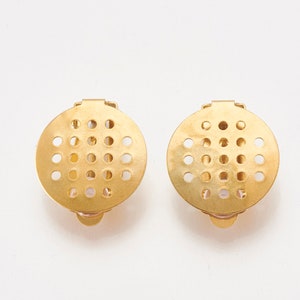 K&ouml;nnte beinhalten: Ein Paar goldfarbene Ohrclips aus Metall mit einem runden Design, das ein Gitter aus kleinen L&ouml;chern aufweist.