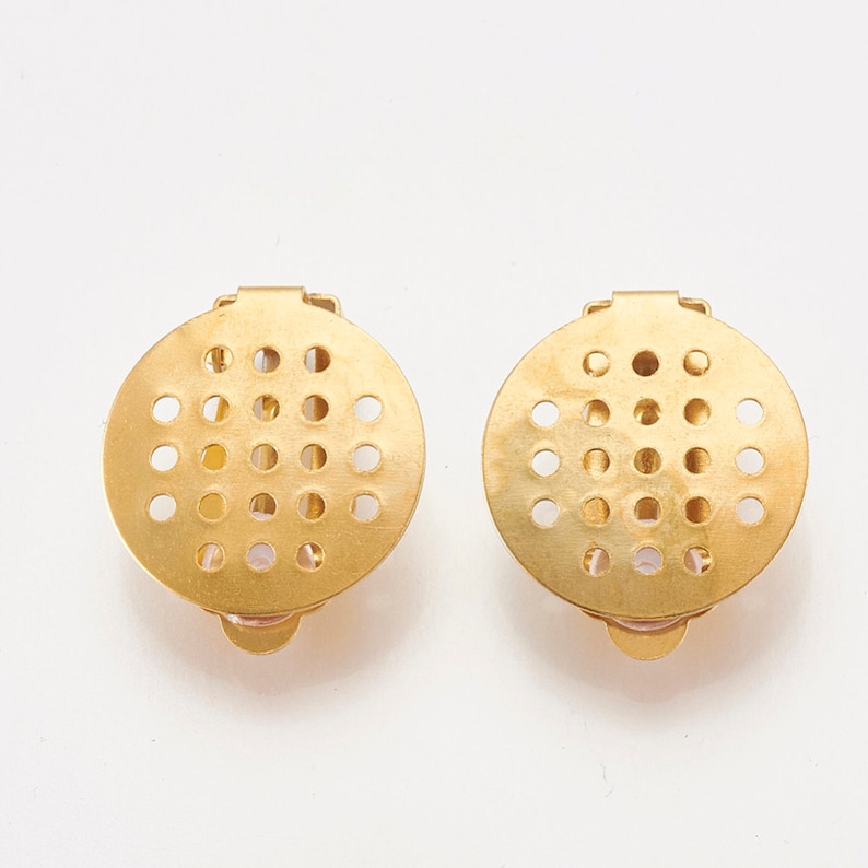 K&ouml;nnte beinhalten: Ein Paar goldfarbene Ohrclips aus Metall mit einem runden Design, das ein Gitter aus kleinen L&ouml;chern aufweist.