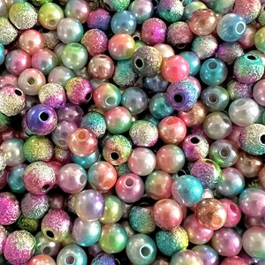 May include: A large assortment of iridescent round beads in various shades of pink, blue, green, and purple. The beads have a textured surface and a hole in the center.