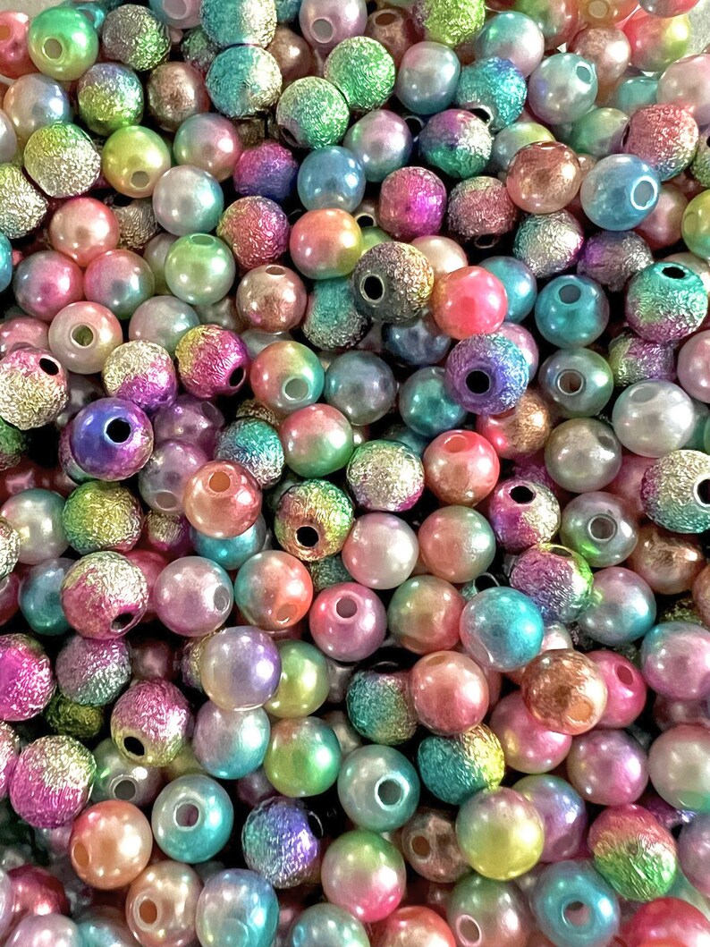 May include: A large assortment of iridescent round beads in various shades of pink, blue, green, and purple. The beads have a textured surface and a hole in the center.