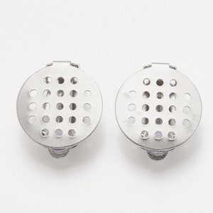 K&ouml;nnte beinhalten: Zwei silberfarbene Metallverschl&uuml;sse mit einem runden, perforierten Design. Jeder Verschluss hat ein kleines, rundes, transparentes Plastikst&uuml;ck in der Mitte.