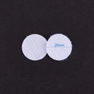 K&ouml;nnte beinhalten: Zwei wei&szlig;e, runde Stoffkreise mit einem Durchmesser von jeweils 20 mm. Die Kreise liegen nebeneinander auf einer schwarzen Oberfl&auml;che.