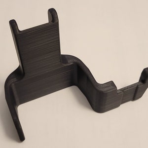 May include: A black 3D printed phone stand with a curved design. The stand has a raised back and a small lip on the front to hold a phone in place.