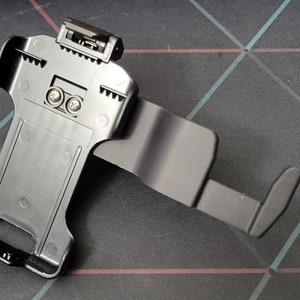 May include: Black plastic phone holder with a swivel arm. The holder has a clip on the back for attaching to a belt or bag.