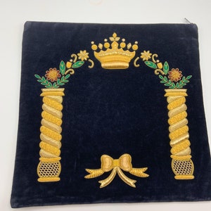 May include: A dark blue velvet prayer shawl with gold embroidery. The embroidery features a crown, two pillars, and a bow. The shawl is a traditional Jewish religious item.