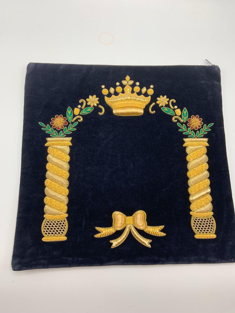May include: A dark blue velvet prayer shawl with gold embroidery. The embroidery features a crown, two pillars, and a bow. The shawl is a traditional Jewish religious item.