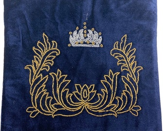May include: A navy blue velvet pouch with a gold and white beaded design. The design features a crown and two symmetrical floral patterns.