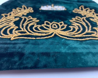May include: A dark green velvet cushion with a gold beaded design. The design features a crown and two symmetrical floral patterns.