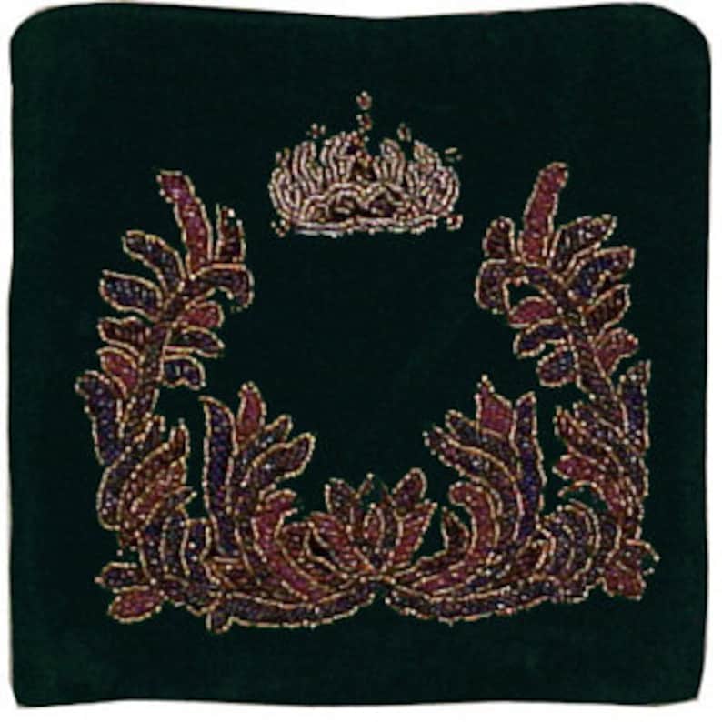 May include: A dark green velvet cushion with a gold and purple beaded design. The design features a crown at the top and a wreath of leaves on either side.