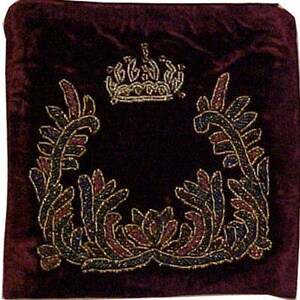 May include: A burgundy velvet pillow with a beaded design featuring a crown and floral motifs.
