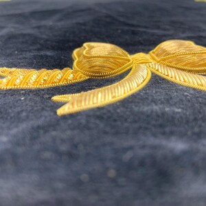 May include: A gold embroidered bow on a dark blue fabric background.