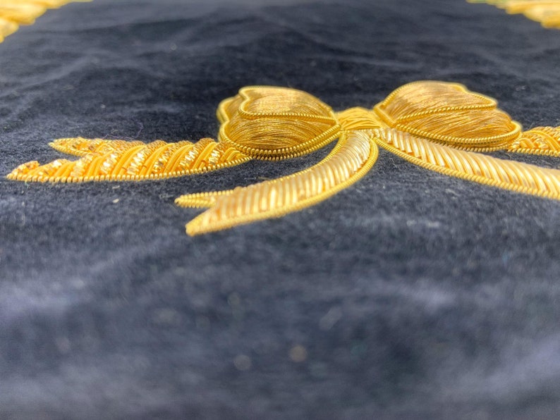 May include: A gold embroidered bow on a dark blue fabric background.