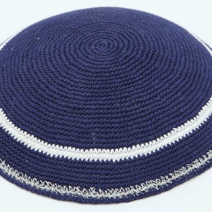 May include: A navy blue knitted kippah with a white trim and a silver edging.