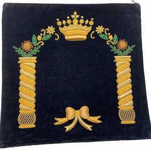 May include: A dark blue velvet prayer shawl with gold embroidery. The embroidery features a crown, two pillars with floral accents, and a bow.