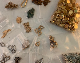 May include: Assortment of gold and silver metal charms and embellishments in various shapes and sizes, including hearts, teardrops, leaves, and geometric shapes, packaged in clear plastic bags.