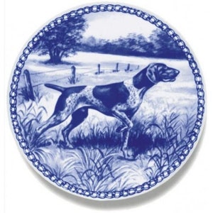 Puede incluir: Un plato de cerámica azul y blanco con un borde de diseño de cadena. El plato presenta una ilustración detallada de un perro Braco Alemán de Pelo Corto corriendo por la hierba alta.