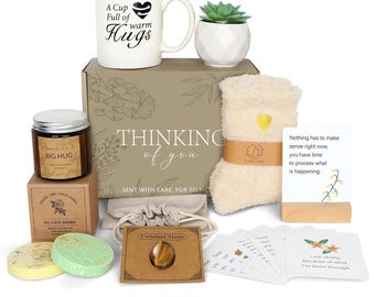 May include: A gift box with a white mug that says "A Cup Full of warm Hugs", a small succulent, a candle, a pair of socks, a comfort stone, and cards. The box says "Thinking of you". The box is beige with floral designs.