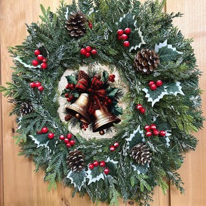 May include: A circular holiday wreath featuring green pine needles, brown pinecones, and clusters of bright red berries. The center displays a decorative circular plaque showing two gold-colored bells tied with a red and black plaid ribbon.