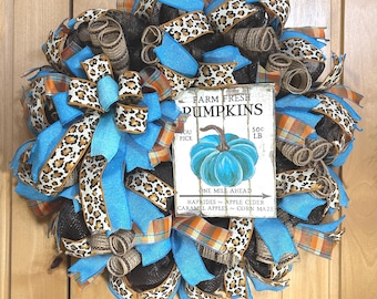 May include: A decorative wreath featuring black, bright blue, and orange plaid mesh ribbons, along with leopard print accents. A rectangular white sign in the centre displays the text FARM FRESH PUMPKINS, YOU PICK 50c LB, ONE MILE AHEAD, HAYRIDES, APPLE CIDER, CARAMEL APPLES, CORN MAZES, and a blue pumpkin illustration.