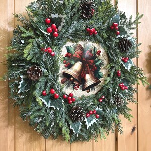 May include: A circular Christmas wreath made of artificial green pine branches, featuring clusters of bright red berries, dark brown pinecones, and white-tipped holly leaves. A central circular plaque displays two gold bells with a red plaid bow.