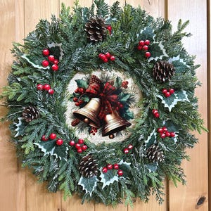 May include: A circular Christmas wreath featuring green pine needles, frosted tips, brown pinecones, and clusters of red berries. The center displays a round plaque with an illustration of two gold bells tied with a red and green plaid ribbon.