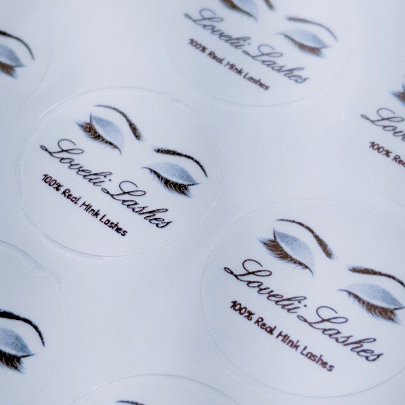 May include: Close-up of several white round stickers with a stylized illustration of a closed eye with eyelashes. The text "Loveli Lashes" and "100% Real Mink Lashes" is printed on each sticker.