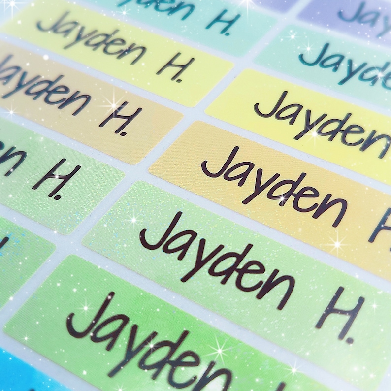 May include: A close-up of colourful, glittery name labels with the name "Jayden H." written in black cursive.