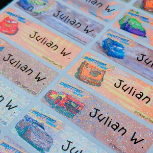 May include: A set of colorful, glittery name labels featuring a cartoon car with the text "Drifting Time" and the name "Julian W." repeated on each label. The labels are designed for children and are perfect for school supplies, lunchboxes, or other personal items.