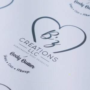 May include: A white label with a black heart shape containing the text "Biz" and the words "CREATIONS LLC HANDCRAFTED BODY PRODUCTS" below. The text "Body Butter Shea. Coco. Mango" is below the logo.