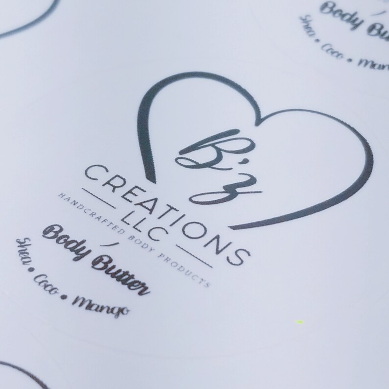 May include: A white label with a black heart shape containing the text "Biz" and the words "CREATIONS LLC HANDCRAFTED BODY PRODUCTS" below. The text "Body Butter Shea. Coco. Mango" is below the logo.
