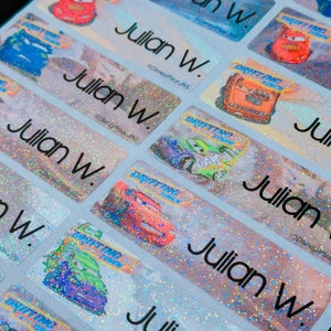 May include: A sheet of colorful, glittery name labels with the name "Julian W." printed on each label. The labels feature a cartoon image of a red race car with the words "Drifting Time" printed on the car.